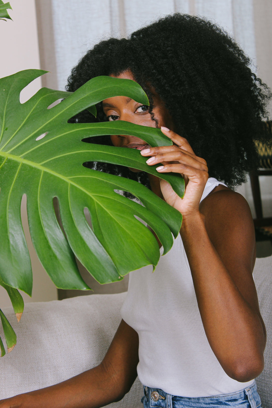 A person peeks through the holes of a Monstera Deliciosa leaf.
