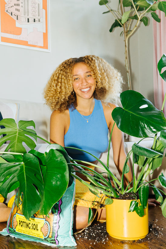 Maryah Greene smiles next to her Monstera Deliciosa, freshly transplanted into a yellow pot.