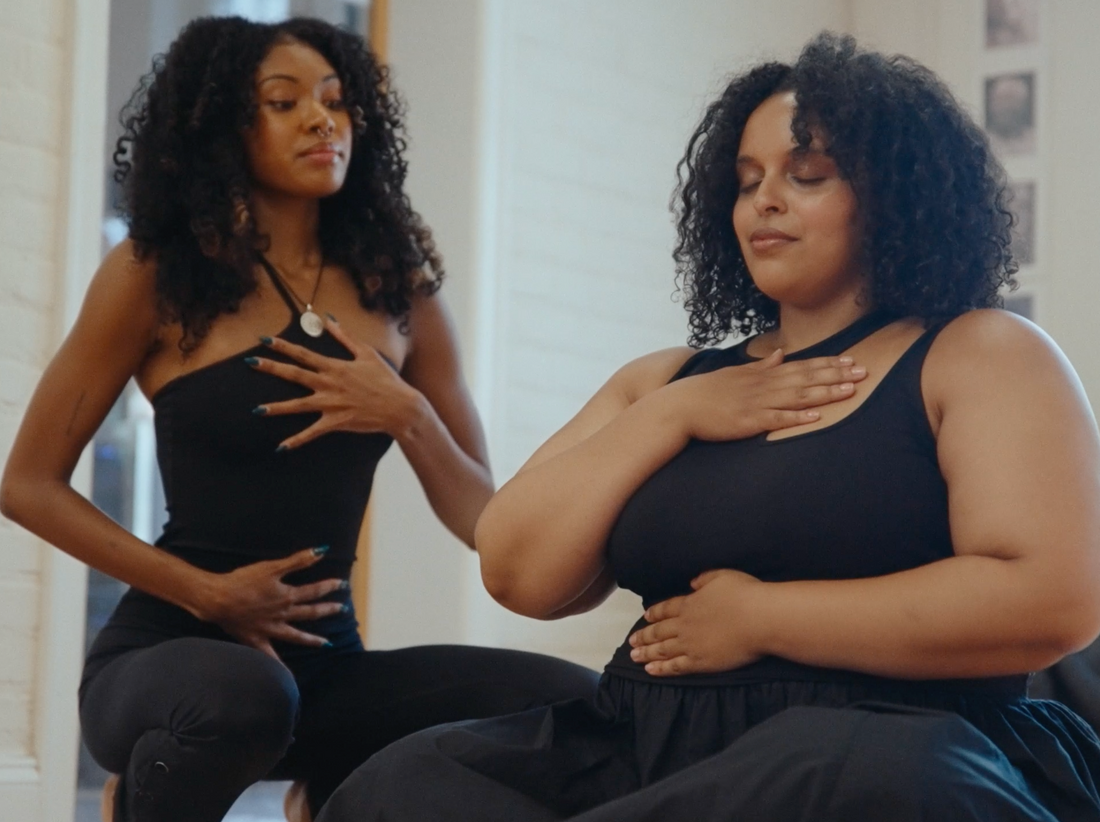 Two women dressed in all black doing deep breathing exercises.